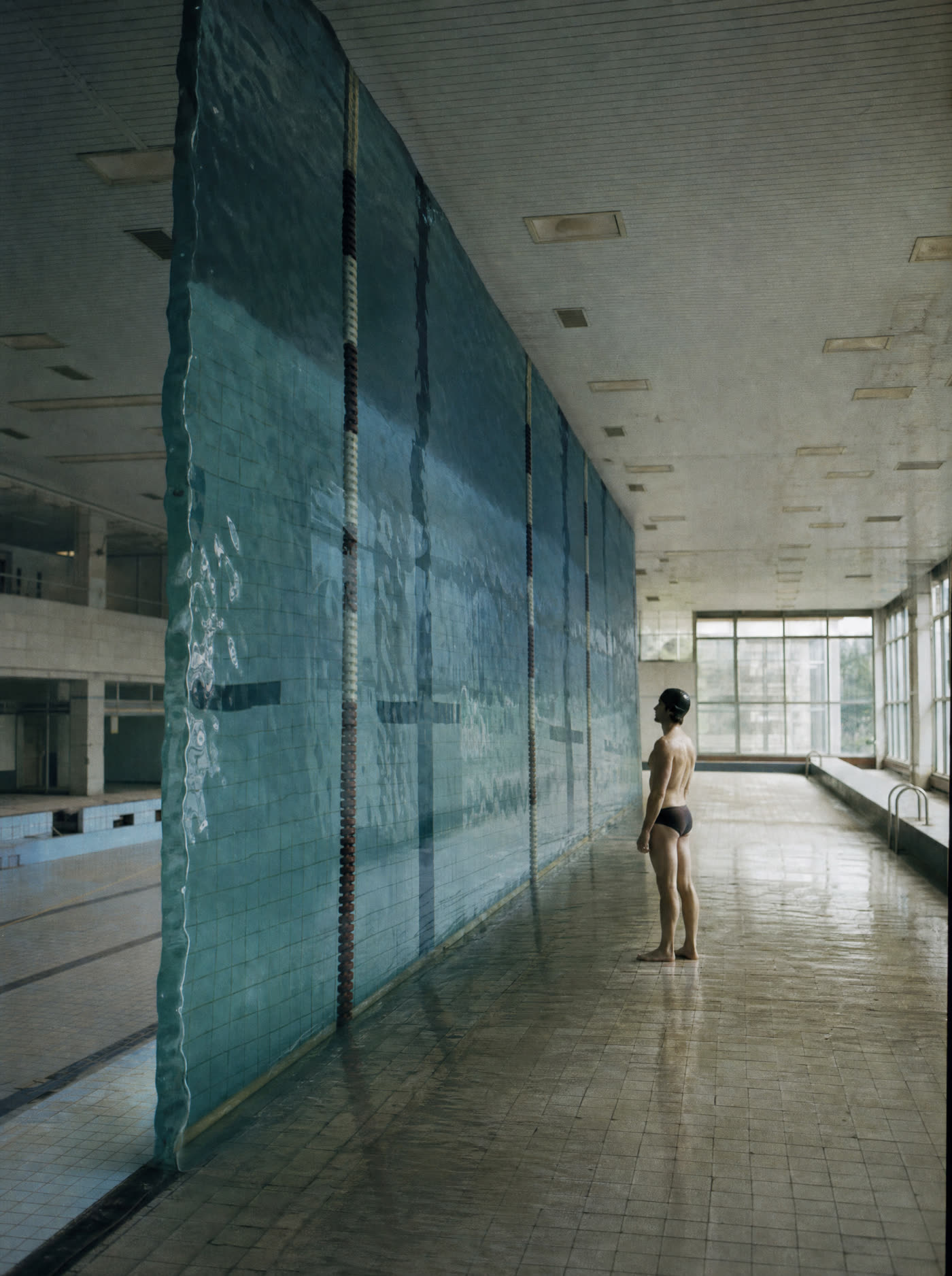 An indoor pool where the water stands upright as a vertical wall, a swimmer beside it