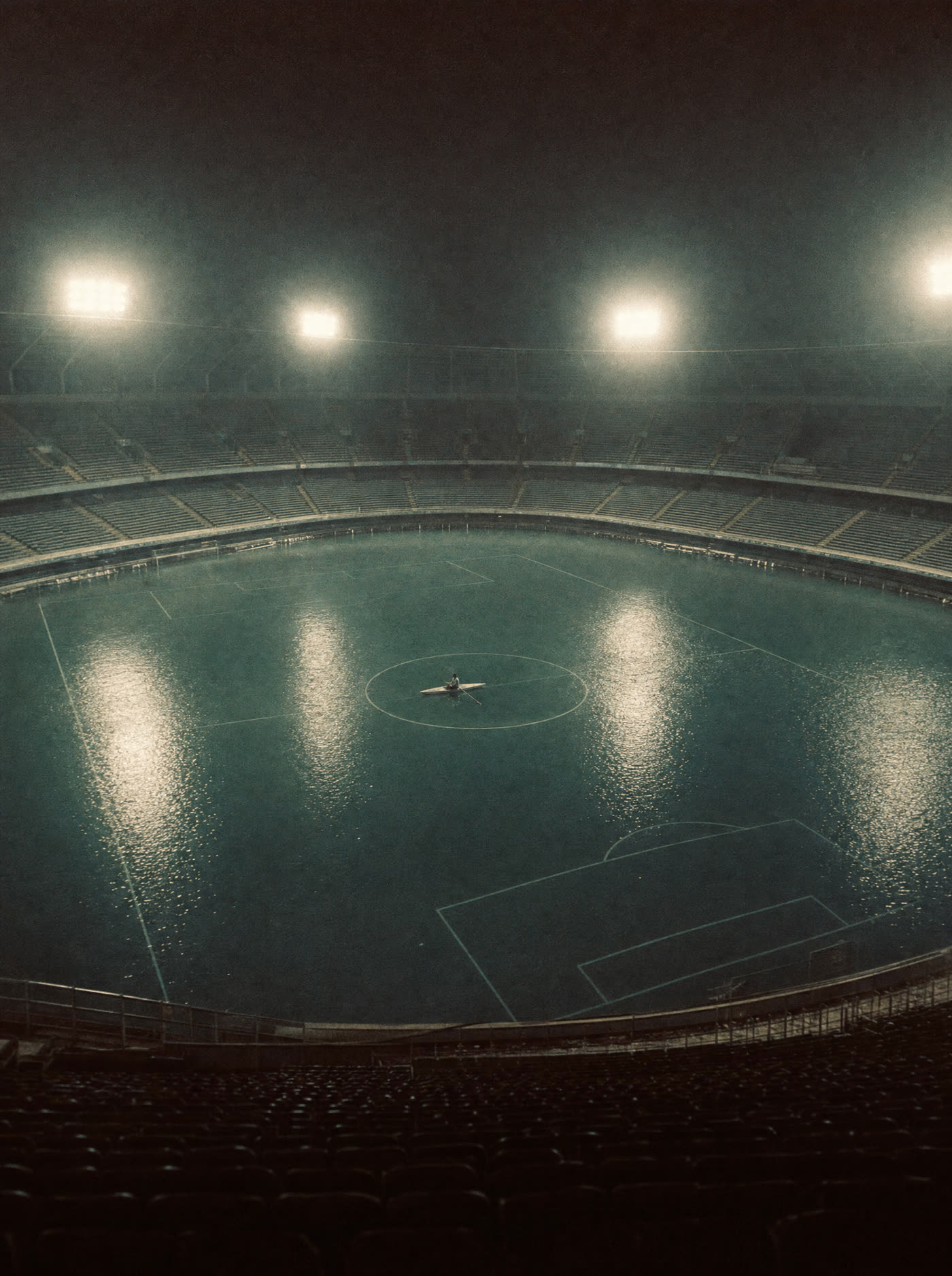 A floodlit stadium filled with still water, pitch markings visible below, a rowing boat in the centre circle